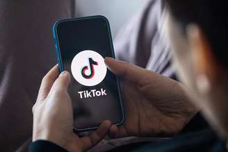 Pessoa de costas usando celular, que mostra logo do TikTok