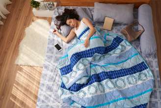 Mulher dormindo sozinha na cama no chão com edredon azul 