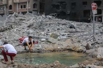 Palestino lava as mãos em uma poça ao lado de um prédio destruído após os ataques israelenses na Cidade de Gaza