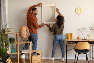 Imagem meramente ilustrativa de um casal arrumando um quadro na sala de casa