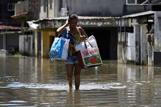 Imagem mostra uma mulher negra caminhando com sacolas por uma rua inunadada no Rio de Janeiro