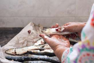 Mulher limpando escamas de peixe de uma sardinha à mão na cozinha de casa