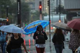 Pedestres caminham com guarda-chuvas na Avenida Paulista em São Paulo em dia de chuva e queda de temperatura.