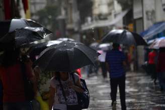 Pedestres se protegem da chuva, com termômetros marcando 23ºC graus, na região central da capital paulista, na tarde desta sexta-feira, 04 de abril de 2025.