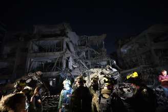 Socorristas e bombeiros israelenses inspecionam as consequências de um ataque com mísseis do Irã perto de Tel Aviv, onde vários carros e edifícios foram destruídos. 