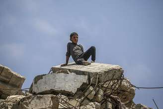 Menino palestino senta-se em escombros após bombardeios no norte de Gaza