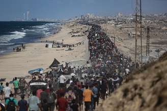 Palestinos, carregando os pertences que conseguiram levar consigo, movem-se em direção à parte norte da Faixa de Gaza pela Rua Rashid, que conecta o norte e o sul do enclave, na Cidade de Gaza