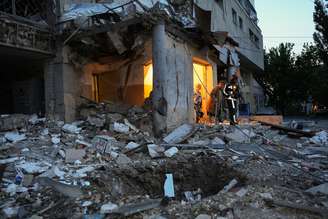 Uma idosa caminha com a ajuda de um socorrista em meio aos escombros de um prédio residencial danificado após um ataque de drone russo em 12 de junho de 2025 em Kharkiv, Ucrânia.