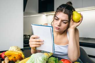 A young woman in the kitchen with a notepad among vegetables, the concept of cooking, dieting and healthy eating.