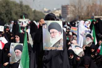 Fiéis em oração em Teerã, com a bandeira iraniana e fotos de Khamenei