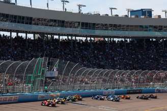 Carros da Indy aceleram diante das arquibancadas lotadas no Phoenix Raceway durante o histórico evento conjunto com a NASCAR