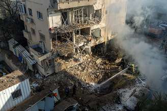 Bombeiros jogam água em uma cratera deixada por um míssil iraniano em 24 de março de 2026 em Tel Aviv, Israel.