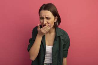 aching pretty caucasian woman puts hand on mouth isolated on pink background with copy space