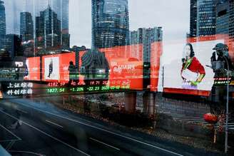 Painel eletrônico mostra os índices de ações de Xangai enquanto as pessoas caminham em uma ponte para pedestres no distrito financeiro de Lujiazui em Xangai, China, em 2 de março de 2026. Foto tirada através de vidro
REUTERS/Go Nakamura