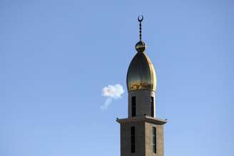 Uma nuvem de fumaça é vista no céu perto do minarete de uma mesquita na cidade de Hebron, na Cisjordânia, Palestina, após uma tentativa de interceptação de mísseis iranianos em 8 de junho de 2026