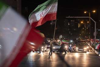 Um apoiador do governo agita uma bandeira nacional iraniana gigante durante um protesto noturno no norte de Teerã, Irã, em 8 de junho de 2026. O protesto é realizado em apoio às recentes operações militares do Irã, que incluíram ataques com mísseis. (Foto de Morteza Nikoubazl/NurPhoto via Getty Images)
