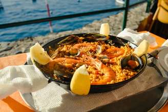 Panela preta servida com o prato paella em uma mesa de frente para o mar.