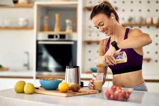 Young happy athletic woman having a fruit smoothie for breakfast in the kitchen.