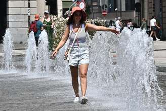 Mulher caminha entre fontes em Gênova para se refrescar de calor