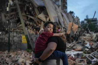 Mulher carrega criança no colo diante de prédio colapsado em Caracas