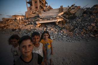 Crianças palestinas posam para foto em meio a escombros em Jabalia, ao norte da Cidade de Gaza