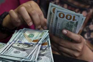 Pessoa conta notas de dólar americano em casa de câmbio em Jacarta, na Indonésia, 9 de abril de 2025. Foto tirada através do vidro. REUTERS/Willy Kurniawan
