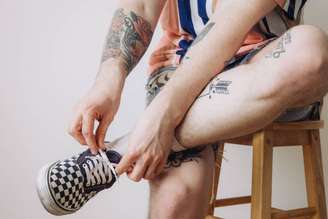 Um homem com tatuagens sentado em um banco amarrando o cadarço do tênis.