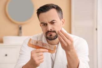 Homem olhando fios de cabelo em um pente de madeira