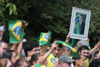 Apoiadores de Flávio Bolsonaro acenam com bandeiras do Brasil e quadro de Jair antes de carreata em Santa Bárbara d'Oeste