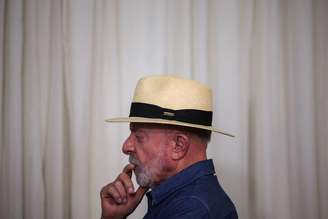 Retrato de Lula, que aparece de chapéu, de perfil, com dedo perto da boca - parecendo pensativo. Ele está dentro de uma sala