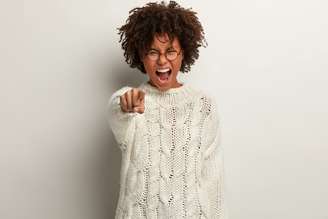 I blame you! Stressful Afro American woman with crisp bushy hair points index finger directly at camera, shouts furiously, expresses annoyance, stands over white background, says you are guilty
