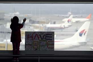 Menina observa os aviões, ao lado de uma placa que diz "temos esperanças", colocada no aeroporto internacional de Kuala Lumpur, na Malásia, nesta segunda-feira, 10 de março