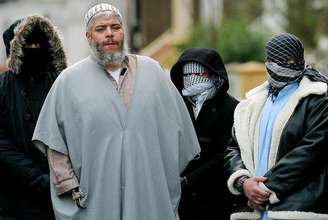 <p>Fotografia de 2003 mostra o clérigo muçulmano Abu Hamza fora da mesquita, em Londres, cercado por apoiadores</p>