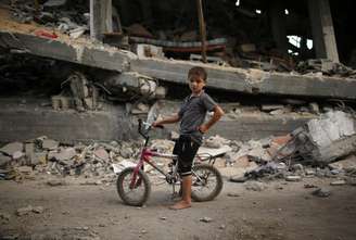 Criança palestina anda de bicicleta em meio aos escombros deixados pelo conflito na Faixa de Gaza