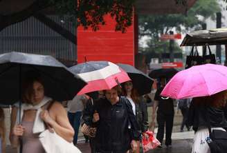 Pedestres caminham com guarda-chuva em tarde chuvosa em São Paulo.
