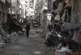 <p>Homem caminha por entre prédios destruídos em uma área sisitada de Homs</p>