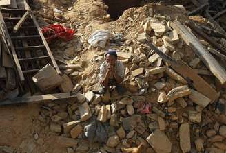 Vítima do terremoto sentado nos destroços de uma casa no vilarejo de Sindhupalchowk