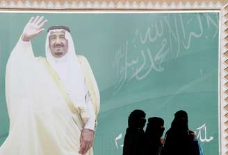 Mulheres passam em frente a poster com o rei da Arábia Saudita Salman bin Abdulaziz Al Saud