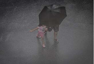 Na imagem, pedestres se protegem de chuva.