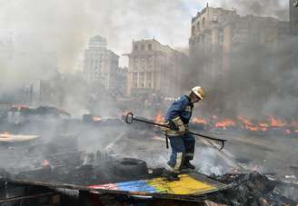 <p>Um bombeiro extingue um incêndio causado pela queima de uma barricada na Praça da Independência, em Kiev, durante confrontos de residentes da capital ucraniana, neste sábado, 9 de agosto</p>