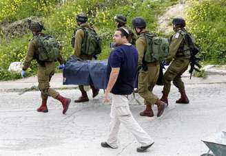 Soldados de Israel recolhem corpos de palestinos mortos por disparos após esfaquear um militar israelense na Cisjordânia. 