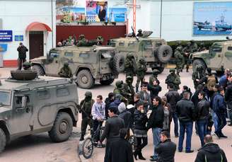 <p><strong>1 de março de 2014 - </strong>Pessoas olham para homens não identificados em uniforme militar bloqueando uma base da unidade de guarda fronteira ucraniana em Balaclava</p>