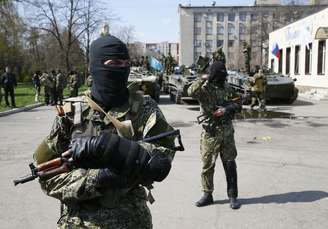 <p>Homens armados, usando fitas pretas e laranja de St. George - símbolo amplamente associado com os protestos pró-russos no país, montam guarda em frente a veículos blindados em Slaviansk, na Ucrânia, em 16 de abril</p>