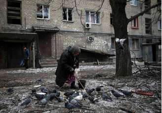 Mulher alimenta pombos diante de casa destruída em Debaltseve, leste da Ucrânia. 05/02/2015.