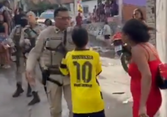Um menino que não aparenta ter mais que 12 anos se coloca entre a mulher e o policial militar