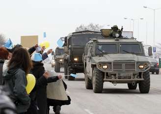 Um comboio militar russo passa por estrada em Simferopol, na Crimeia, neste sábado, enquanto manifestantes contra a guerra protestam