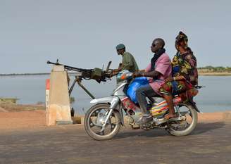 Homens em uma motocicleta passam por um soldado do Exército do Mali protegendo uma ponte sobre o rio Niger