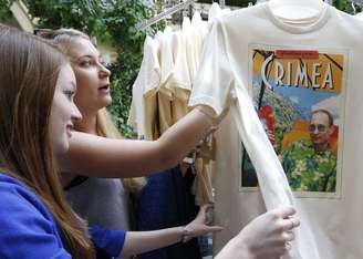 <p>Mulheres observam camisetas com imagens do presidente da Rússia, Vladimir Putin, que estão à venda na Gum, loja de departamentos no centro de Moscou, em 11 de junho. Popularidade do presidente aumentou após anexação da península da Crimeia, em março</p>