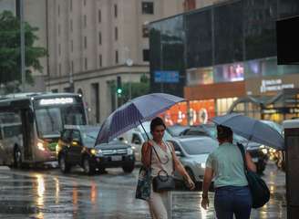 Pedestres caminham com guarda-chuva na Av. Paulista em São Paulo em dia de precipitação e queda de temperatura.
