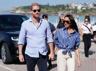 Harry e Megan de mãos dadas durante um passeio. Eles estão usando óculos escuros